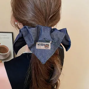 Blue denim bow hair claw clip with bear label and rhinestones worn on a woman's hair