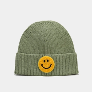 Gros plan du bonnet en tricot vert sauge avec écusson smiley jaune brodé en bouclette
