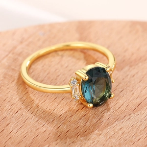 Macro shot of oval green gemstone ring with side diamond accents on wood surface