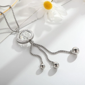 Detail of silver long necklace with crystal ring pendant and metal ball tassels on white desk