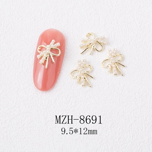 Macro view of 3D bow nail art charm with pearls and gold alloy on a soft pink nail