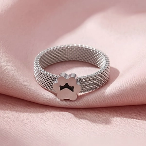 Close-up of silver mesh ring with a cat paw design resting on soft pink silk fabric