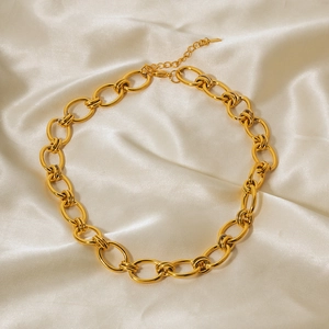 Détail d'un collier à grosse maille dorée avec fermoir mousqueton sur tissu en soie