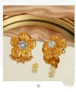Close-up of golden flower stud earrings with central crystal on silk background