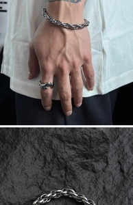 Detail of silver heavy chain bracelet and textured ring on a dark rock background