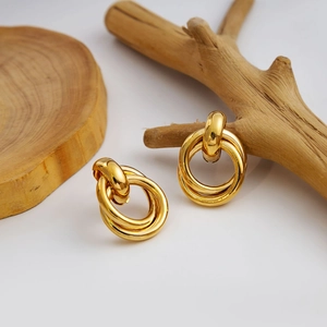 Close-up of golden triple-interlocked geometric hoop earrings on a minimalist wooden base