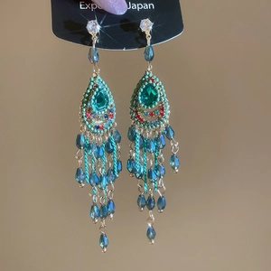 Detail of bohemian long tassel earrings with green pear-shaped stone and blue beads