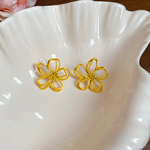 Detail shot of yellow flower shaped hollow earrings placed in a white ceramic shell bowl