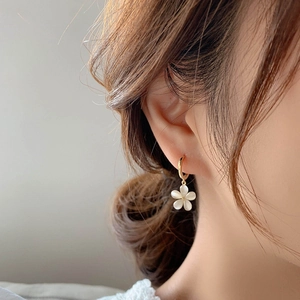 Elegant gold flower earrings with white cat eye stone petals worn by a model