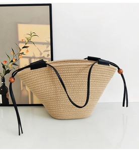 Detail of woven straw tote bag with black leather handles and wooden bead drawstring
