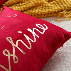 Close up view of red velvet throw pillow cover with gold foil letter print details.