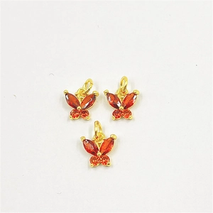 Détail de trois pendentifs papillons dorés sertis de zircons cubiques rouge et orange