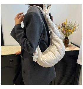 Detail of white quilted dumpling bag featuring knot strap and plush doll pendant