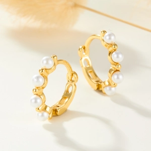 Close-up of S925 silver gold hoop earrings with small pearl inlays on a beige background