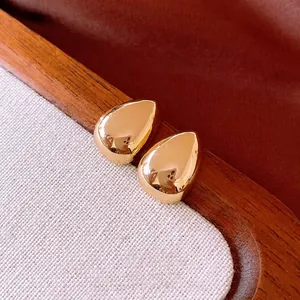 Polished gold waterdrop earrings with teardrop shape on warm textured background