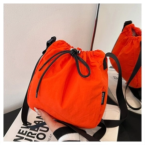 Close-up of bright orange nylon drawstring bucket bag with black strap and brand tag