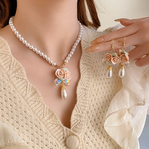 Close-up of elegant floral necklace and earrings set with pink roses and teardrop pearls