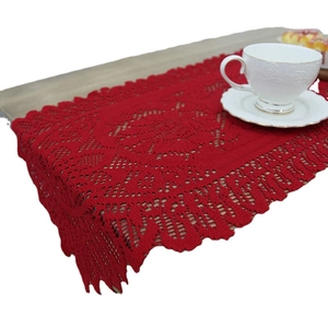 Red lace Christmas table runner with hollow patterns and fringe on a wooden table