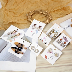 Artistic jewelry display card with assorted golden earrings and resin hair clips on paper