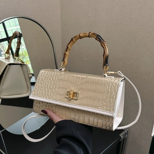 Detailed side view of beige crocodile embossed bag with iconic bamboo handle and gold hardware