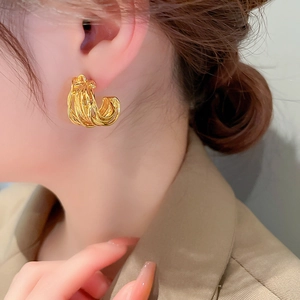 Close-up of a model wearing a wide gold-colored C-shaped earring with multi-layered lines