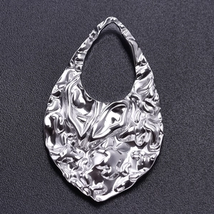 Macro detail of silver-tone teardrop pendant with a unique hammered texture on black background