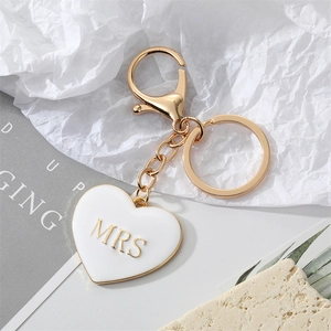 Minimalist gold heart keychain with white enamel Mrs lettering on stone background