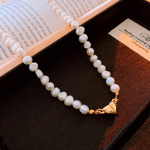 Macro shot of irregular baroque pearls and a polished golden heart charm on a vintage book