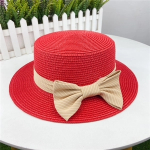 Detail of red straw sun hat with beige striped ribbon bow on flat brim beach cap