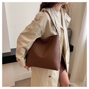 Brown woven shoulder bag shown on model with beige trench coat for high-capacity daily use