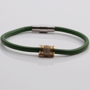 Dettaglio del bracciale in pelle verde con perla dorata traforata e chiusura magnetica
