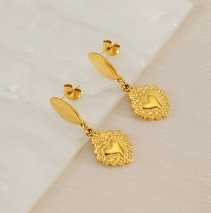Detailed macro of gold stainless steel heart earrings on an artistic white ripple background