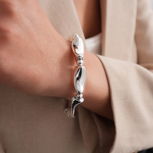 Close-up of chunky silver geometric linked bracelet on a model wearing a beige blazer