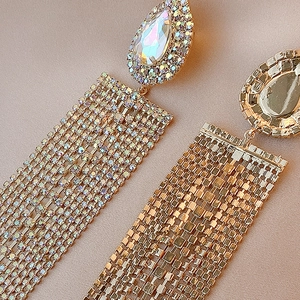 Detailed close-up of golden teardrop tassel earrings with sparkling rhinestones on silk