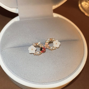 Macro detail of asymmetric gold floral earrings with ladybug and rhinestone accents