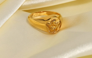 Macro detail of gold 18k plated stainless steel ring with cupid angel emblem on silk
