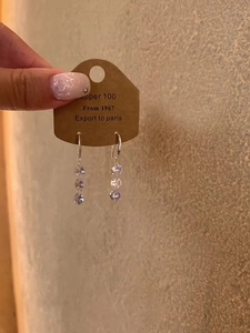 Close-up of dangling silver earrings with three round cubic zirconia on a kraft card