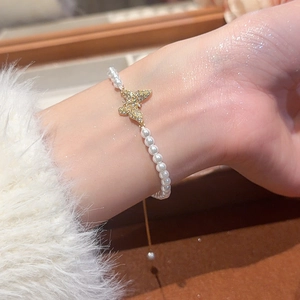Detailed close-up of a pearl bracelet with a gold butterfly charm on a woman's wrist