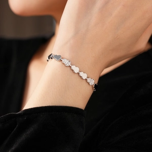 Detailed view of glossy heart and textured gourd charms on a silver bracelet worn on wrist