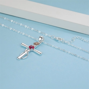 Detail of silver cross necklace with red gemstone and rose gold flower on blue background