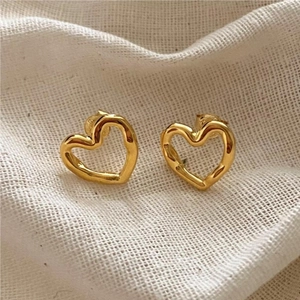 Detailed close-up of golden hollow heart studs with hammered texture on beige linen