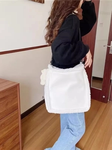White faux fur tote bag with teddy charm and black strap shown on model in home setting