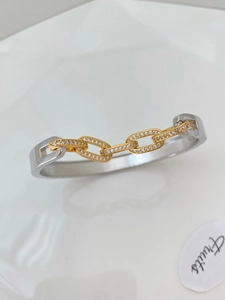 Detail of silver C-shaped cuff featuring a gold chain center set with zircons