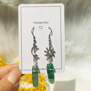 Macro detail of sun and moon earrings with wire-wrapped green raw stones on cards