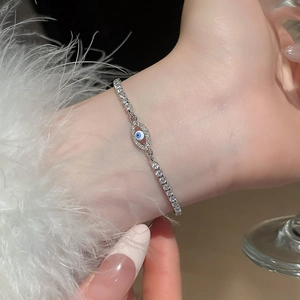 Close-up of a silver Evil Eye bracelet with zircon stones worn by a model on feathers