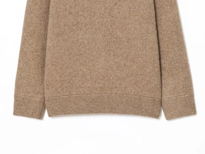 Detail of camel marl knit sweater showing rib-knit hem and cuffs on a white background