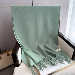 Close-up of green cashmere-feel scarf with fringe and vintage brand label on a chair