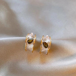 Detail of French style earrings with teardrop green zircon and textured gold edges
