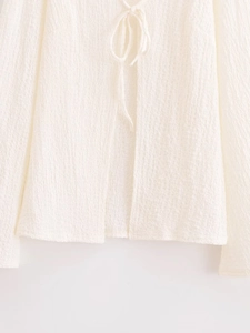 Detailed view of white textured fabric and drawstring tie front design on the summer top