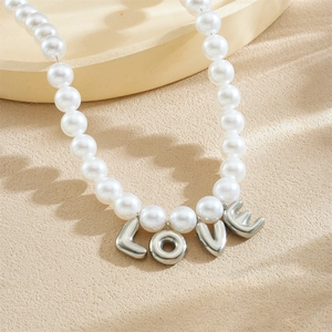 White pearl necklace with silver LOVE letter pendant on a beige textured background